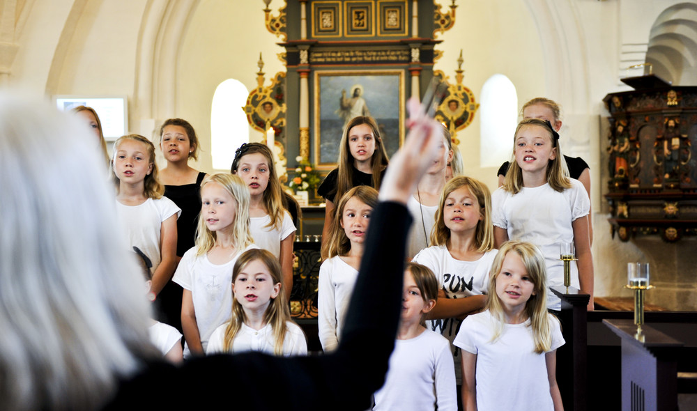 Korleder dirigerer et pigekor, der står foran alteret i en kirke